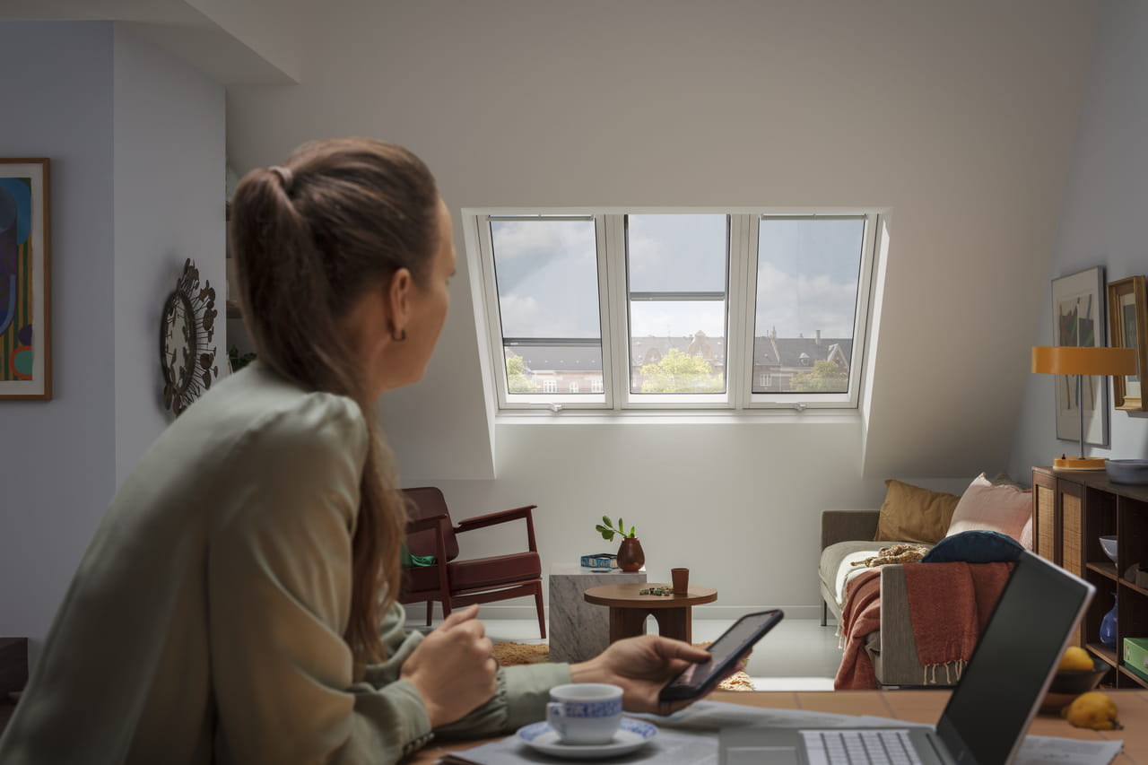 Woman sitting in her home using VELUX Touch to control her VELUX blinds on her roof windows