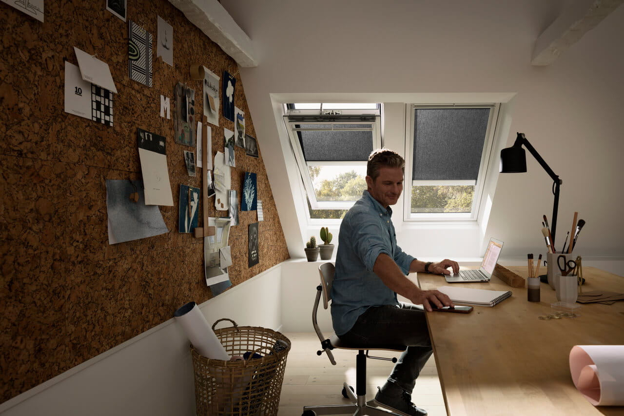 A man sitting at the desk in the home office with VELUX roof windows and blinds