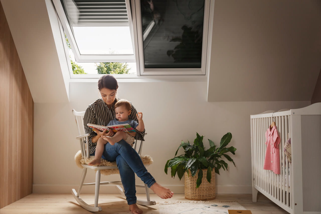 Woman sitting in a kids room with a baby on her lap. She is reading book to the baby.