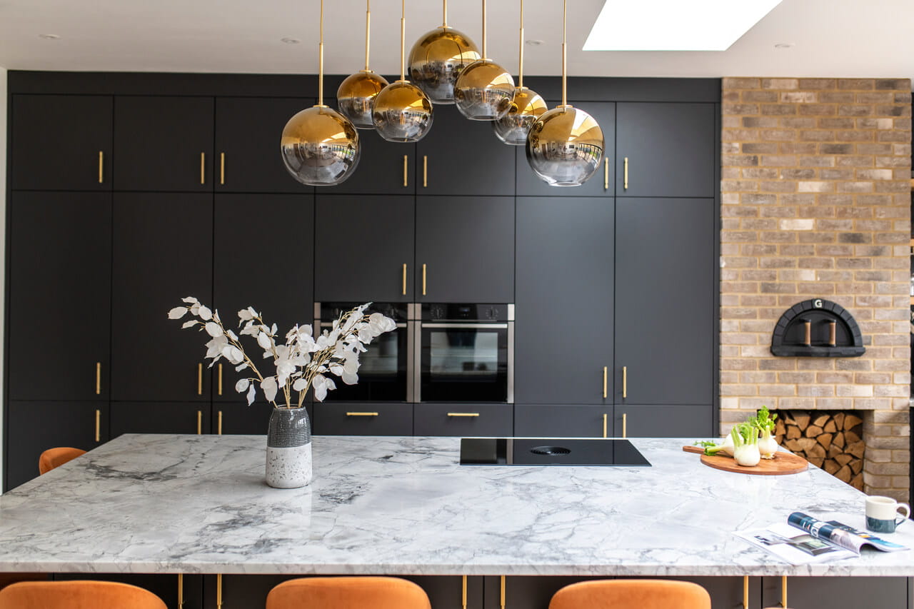 A dark painted kitchen with golden details and marble table top