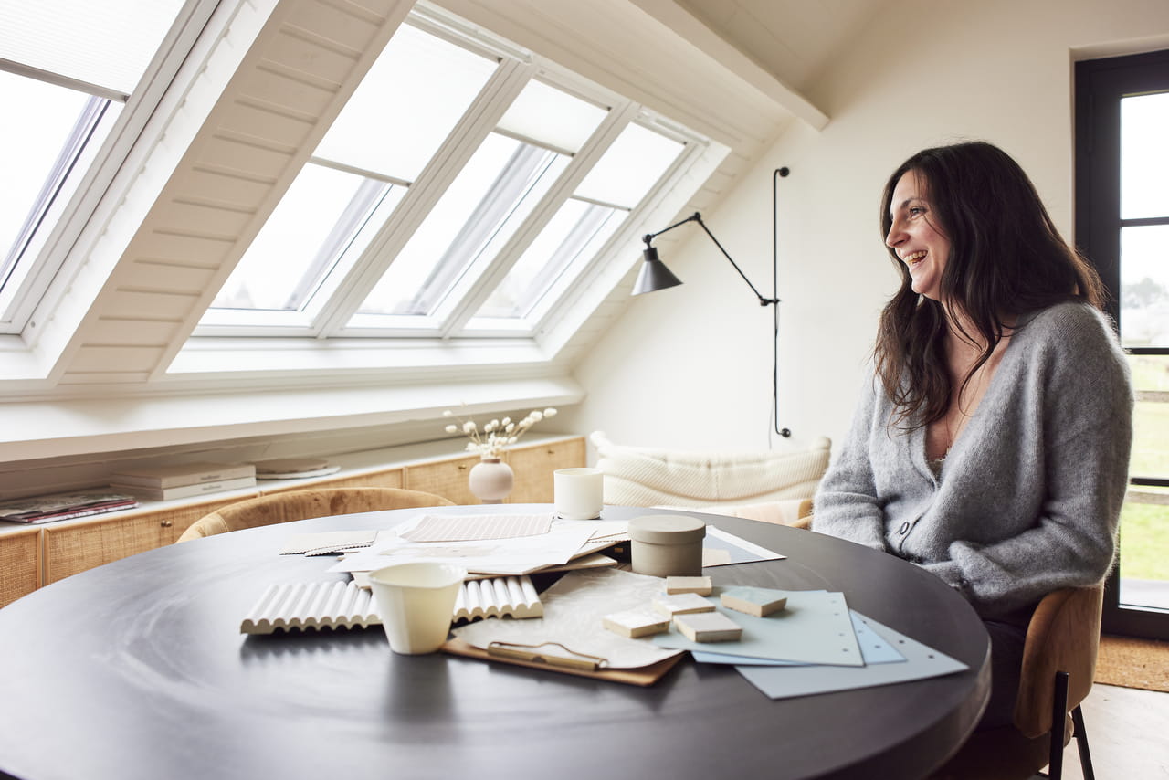 Woman sitting at desk looking at her VELUX roof windows with blinds