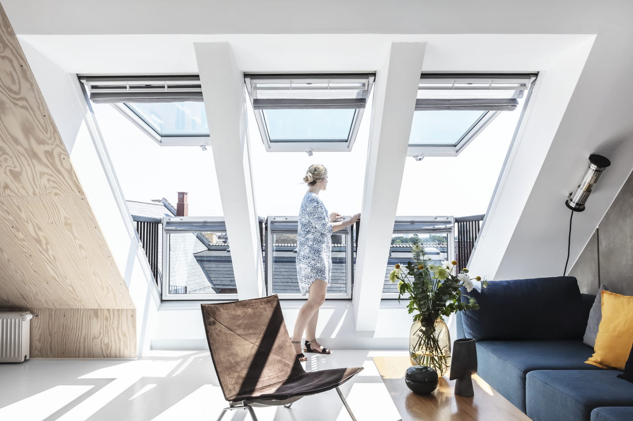 Woman standing by window in bright living room with three VELUX roof windows