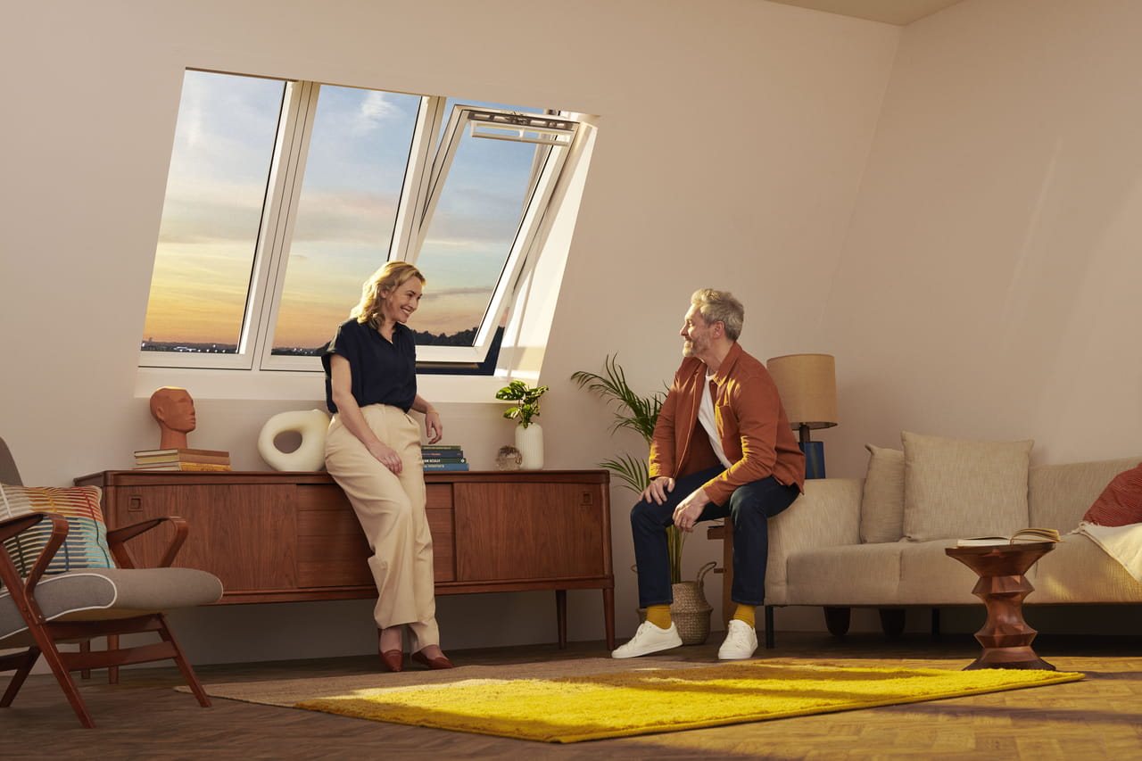 Man and woman sitting in their livingroom underneath VELUX 3-in-1 windows