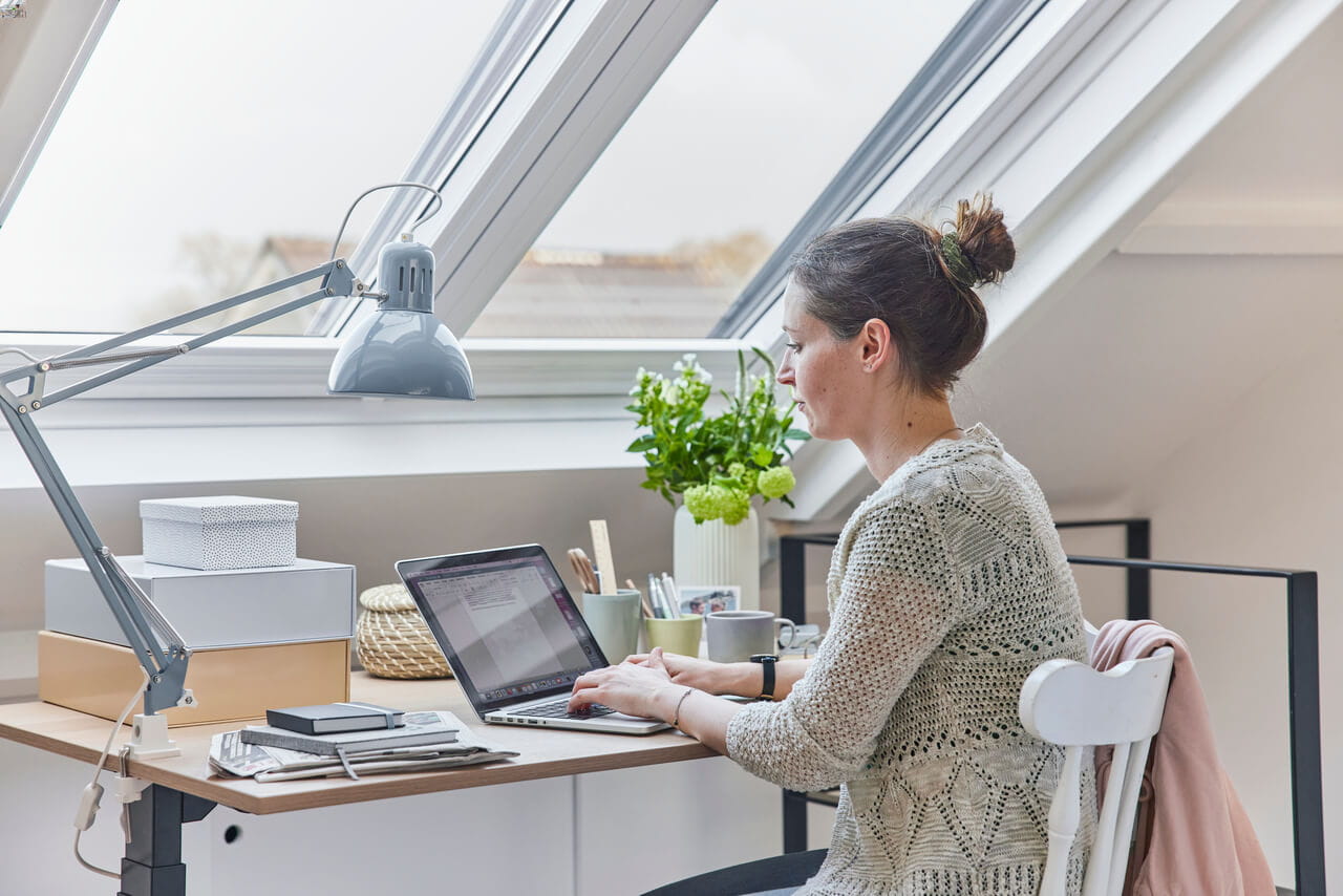 A woman sitting by the roof window and working with a laptop