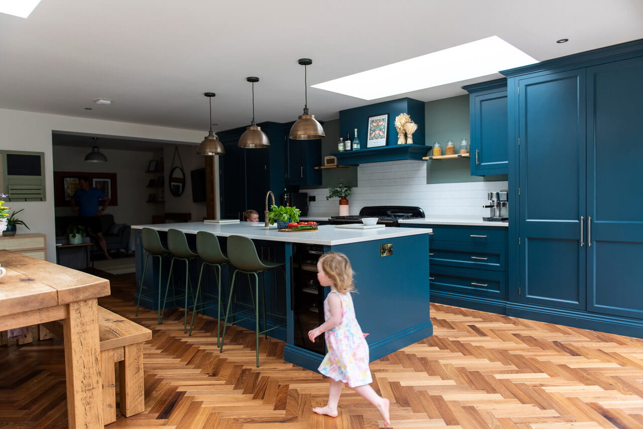 A young toddler running in the spacious and bright blue painted kitchen.