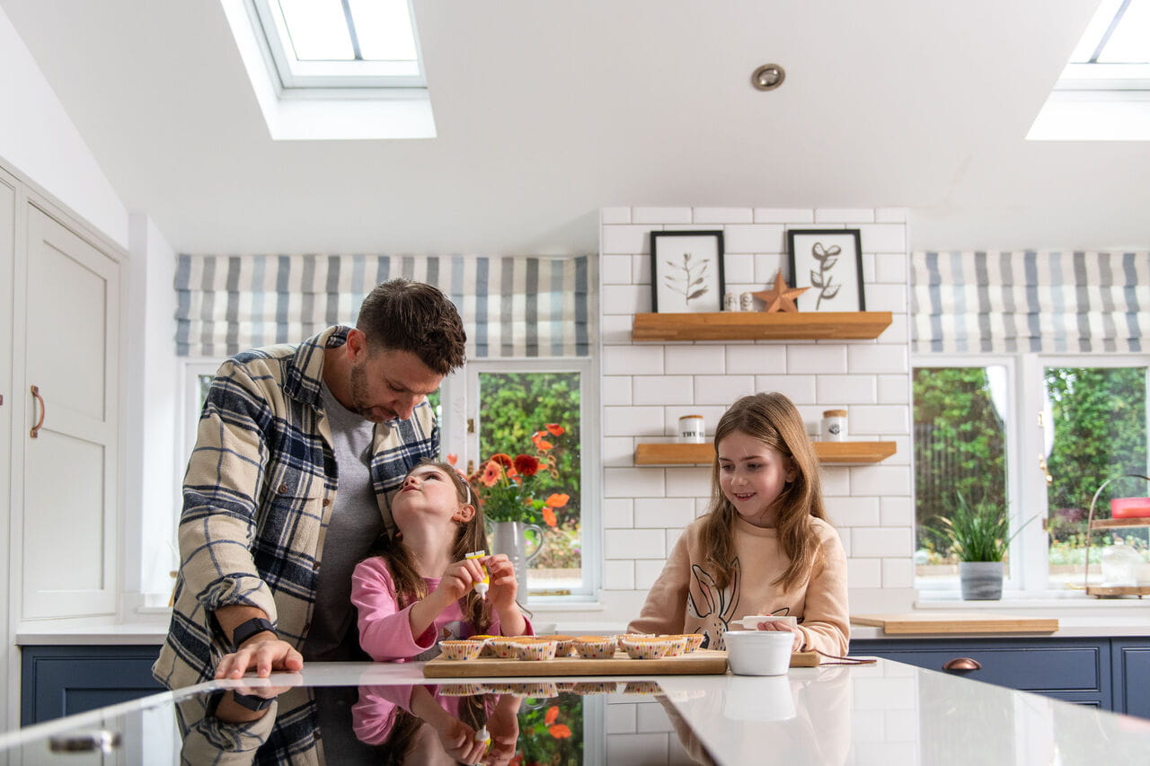 Father with his two daughters standing in their bright kitchen with VELUX roof windows