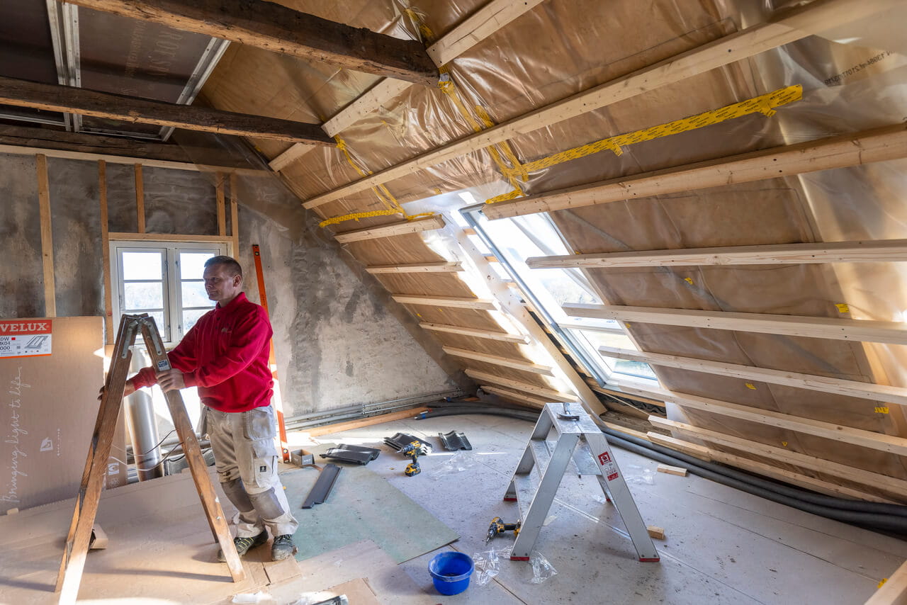 A handyman standing with ladder in the attic under construction
