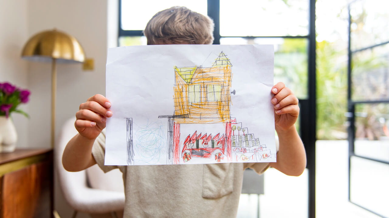 A kid is holding his painting of a house.