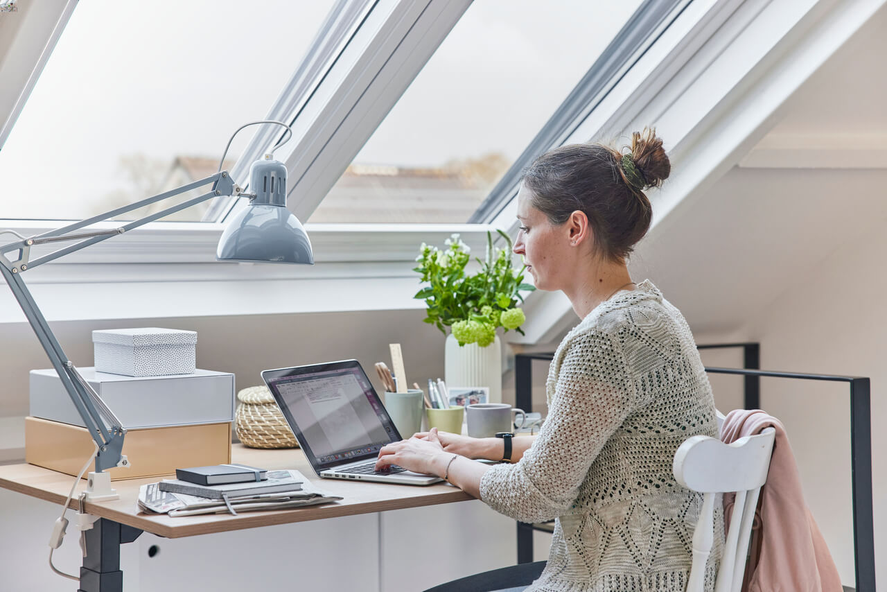 Woman sitting by the roof window and working on a laptop in the home office"