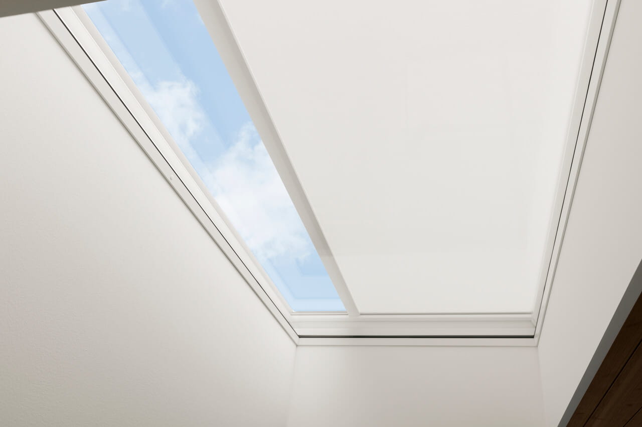 Image of a VELUX flat roof window with anti-heat blinds partially rolled down.