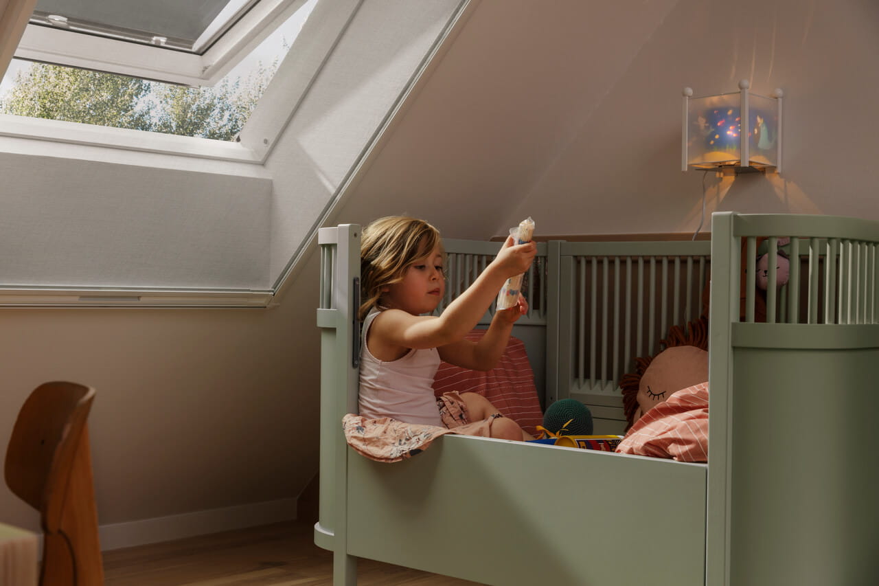 Child playing in a room next to a VELUX roof window with anti-heat blinds.