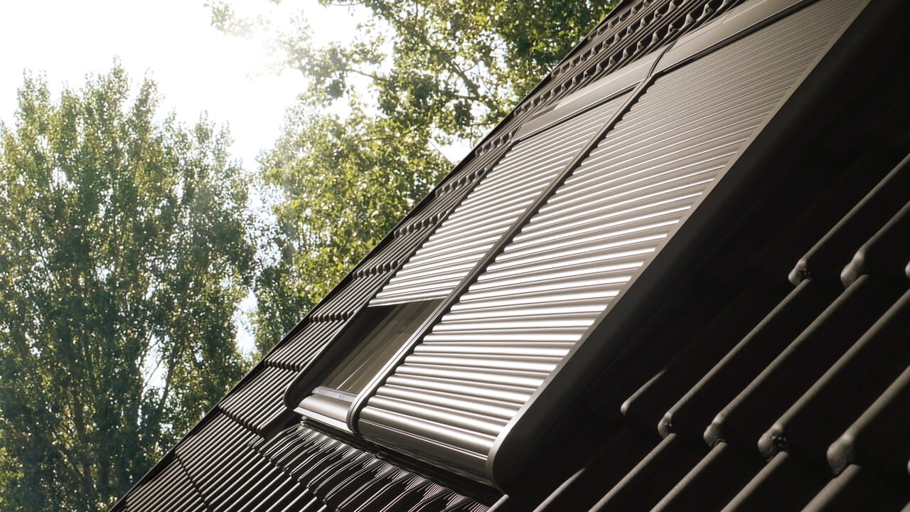 Exterior image of a black roof with 2 VELUX roller shutters installed, one partially opened.