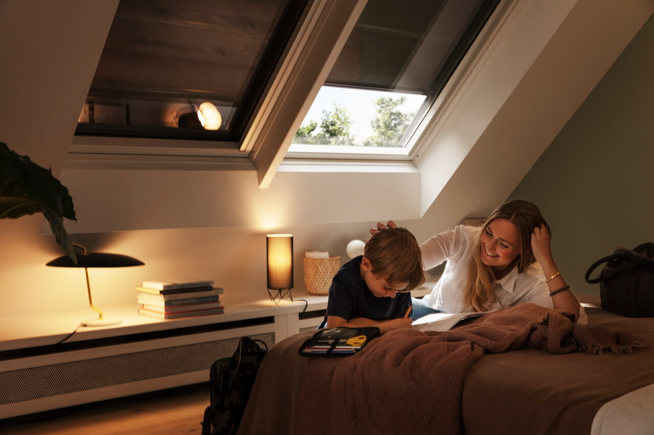 Person talking to a child on a bed, VELUX roller shutters control the light and heat coming into the room
