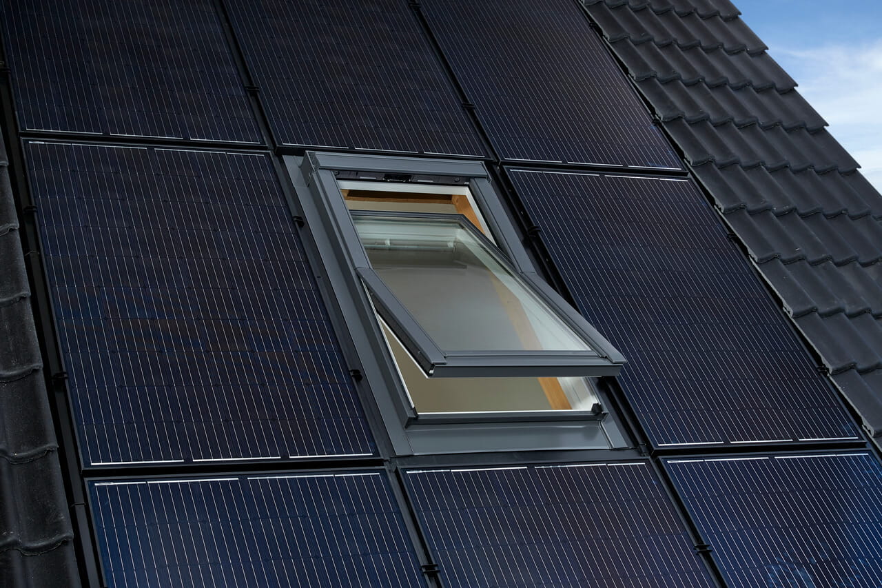 An outside view to a roof with on roof window surrounded by solar panels.