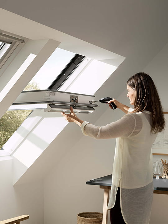 Person holding an electrical screwdriver up to a VELUX roof window side by side solution