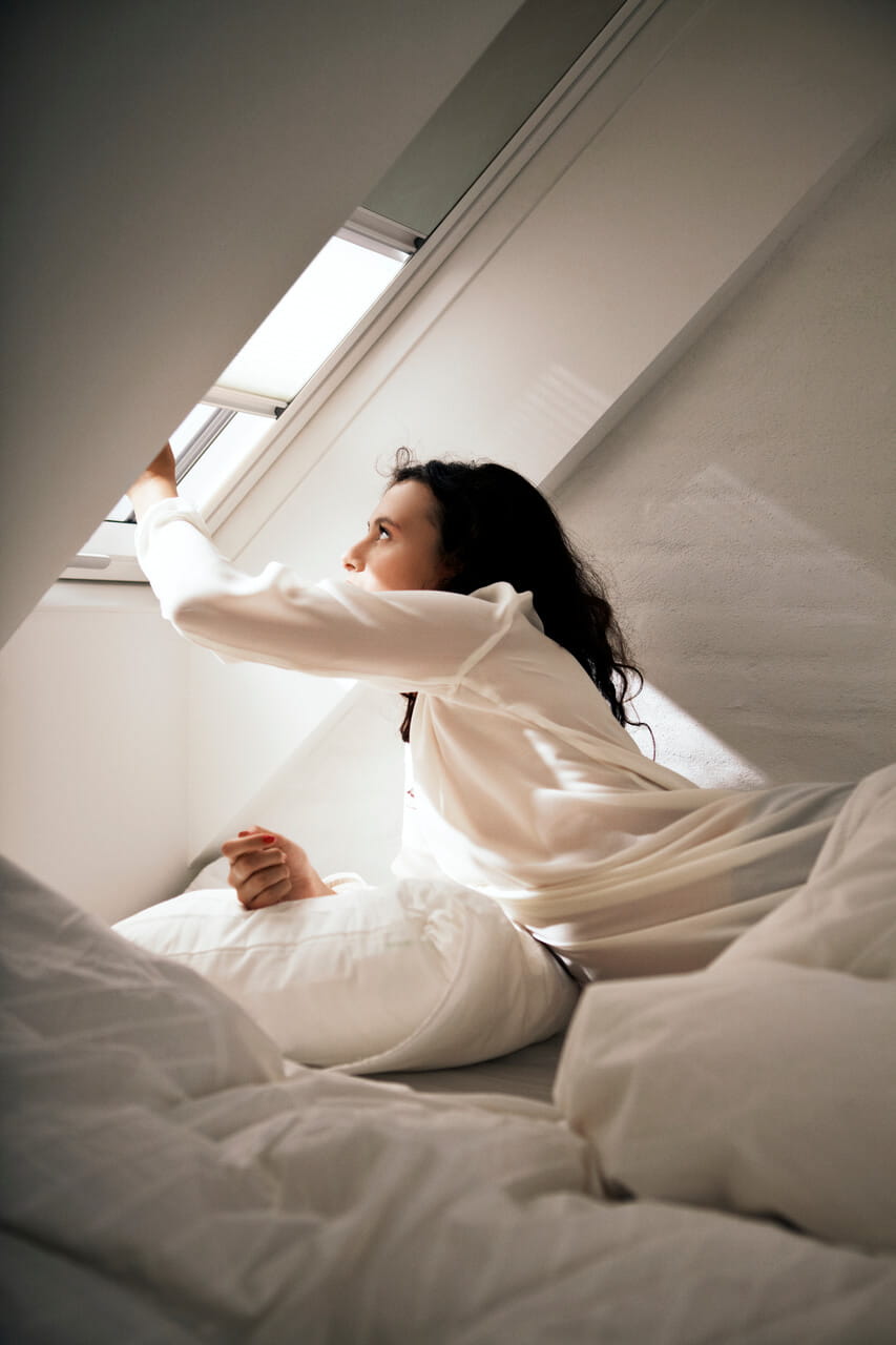 Person lying on a bed while pulling a VELUX Duo blind down to block out the light.