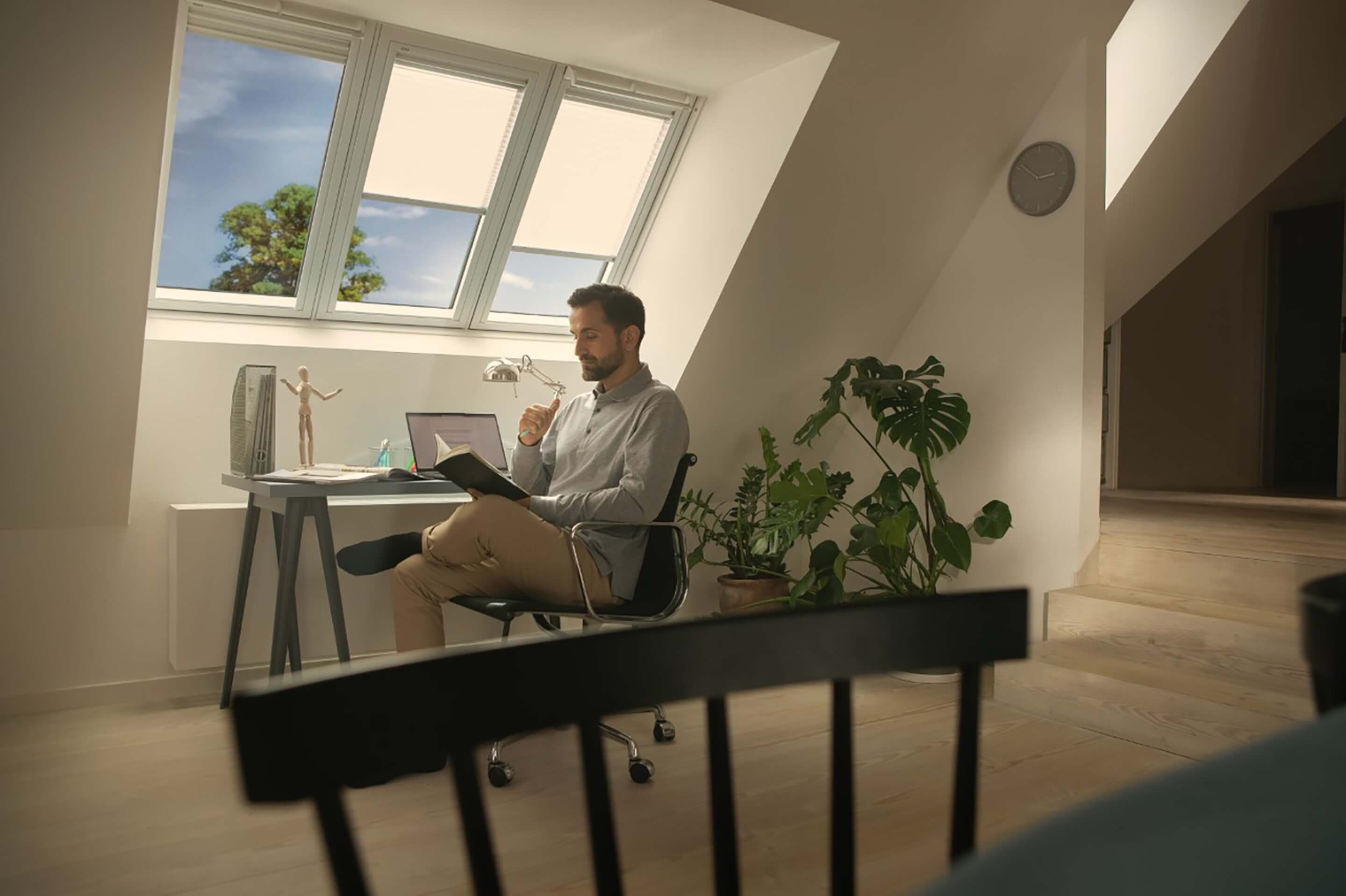 Man sitting at a desk with VELUX roof windows and blinds in the background