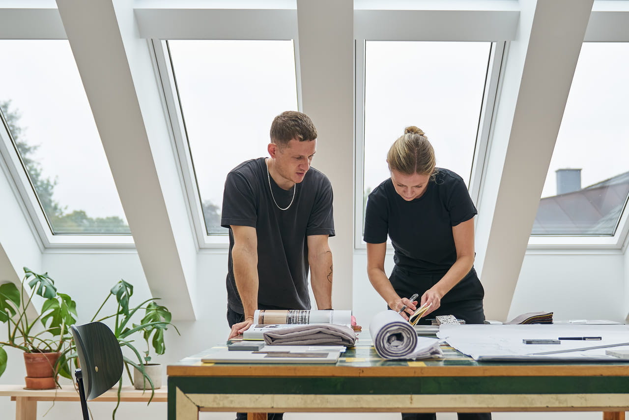 Two people working at a table in front of a multiple installation of VELUX roof windows