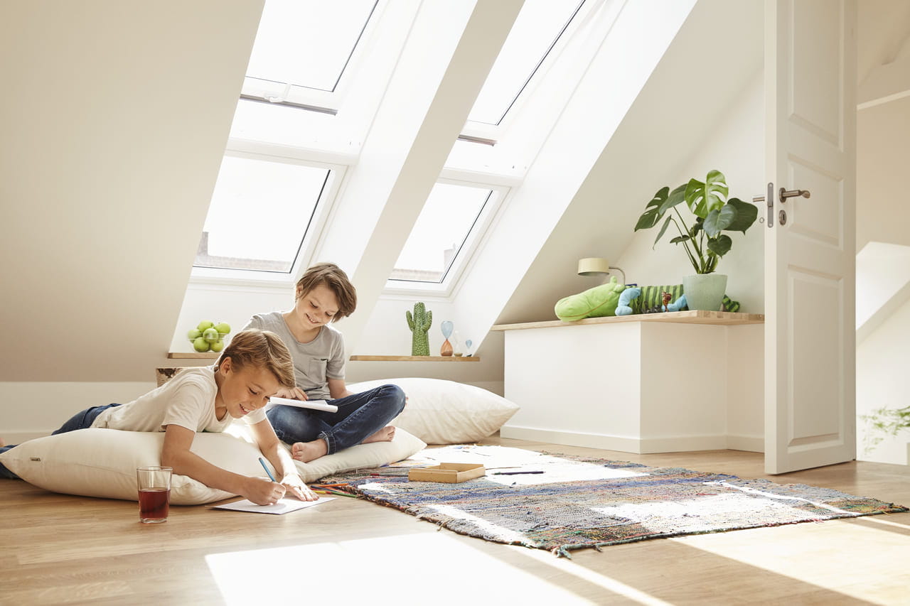 Two kids playing on the ground in the attic with roof windows