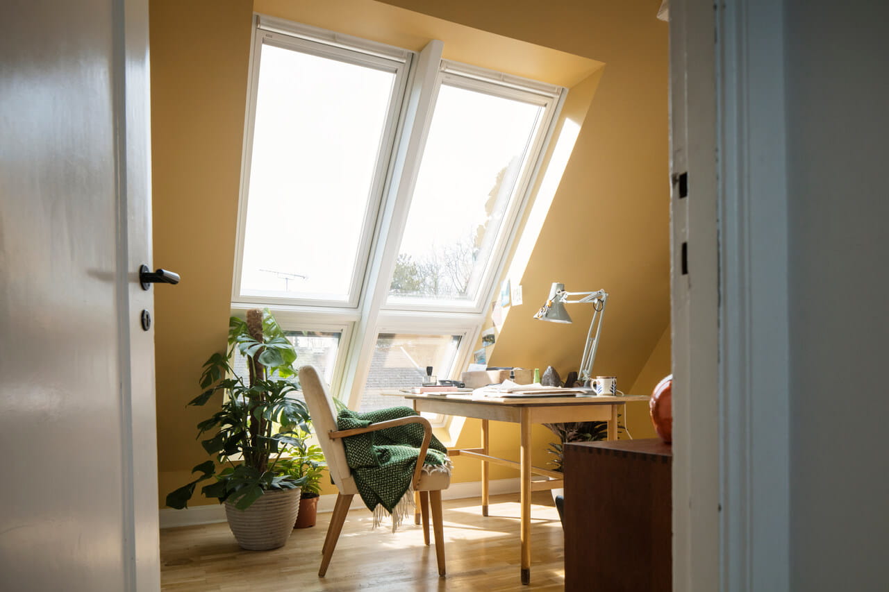 A home office in the attic with yellow painted walls and a big roof window