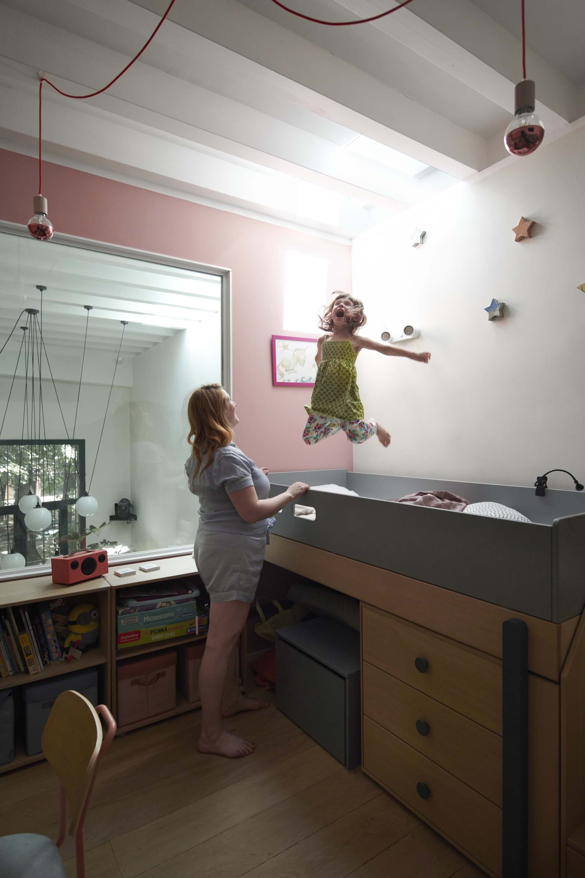 A girl jumping on the bed. Woman standing next to the bed.