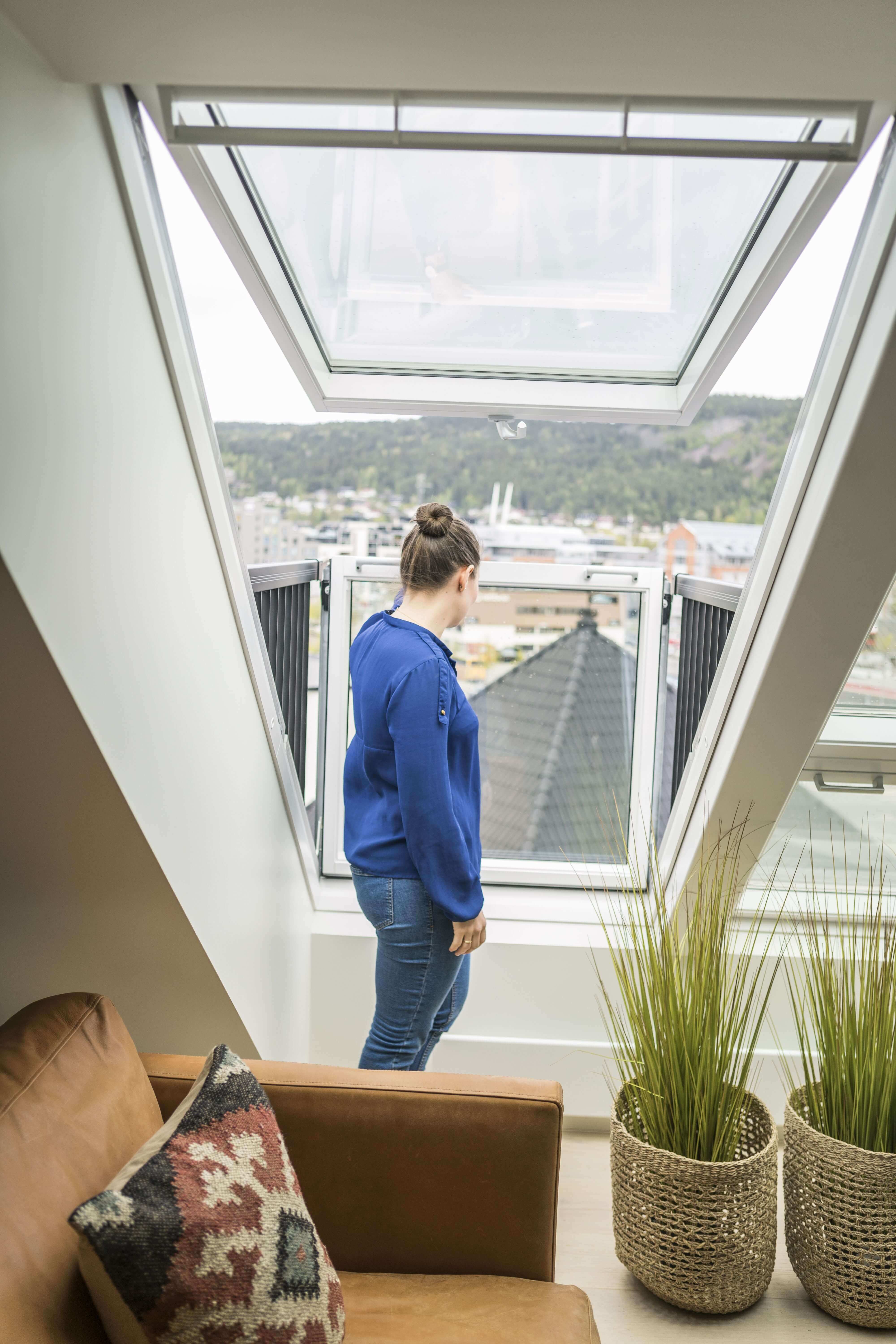 Woman in a blue blouse looking outside through the VELUX Cabrio roof window