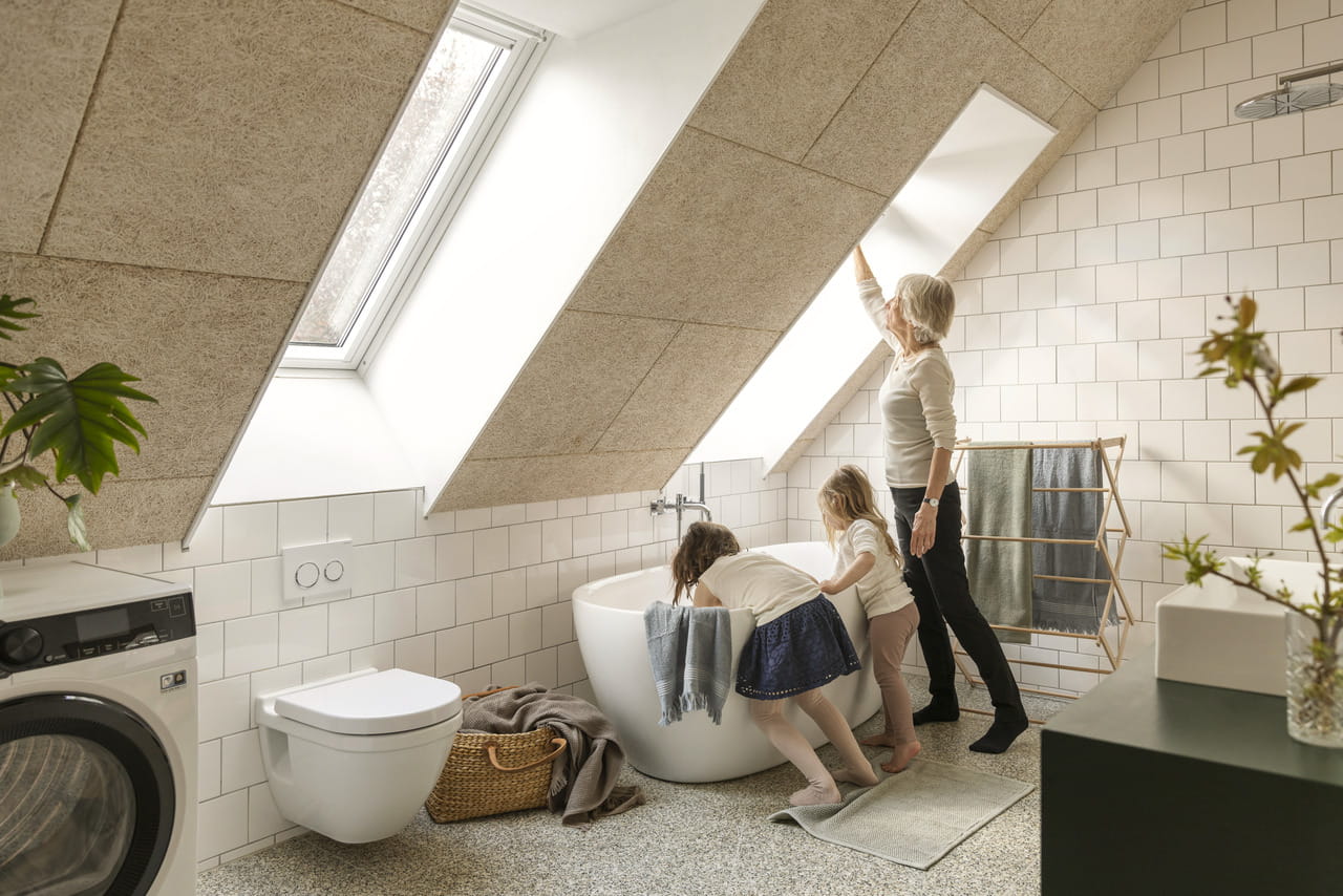 Woman and two kids in the bathroom, standing next to the bath tub.
