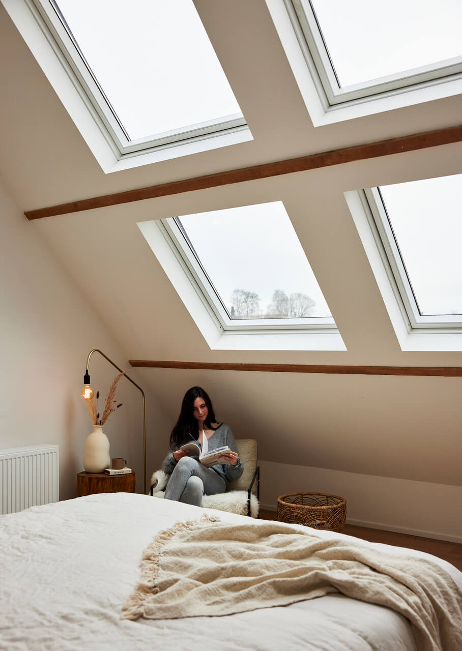 Woman reading a book while sitting in the chair and with roof windows above her.