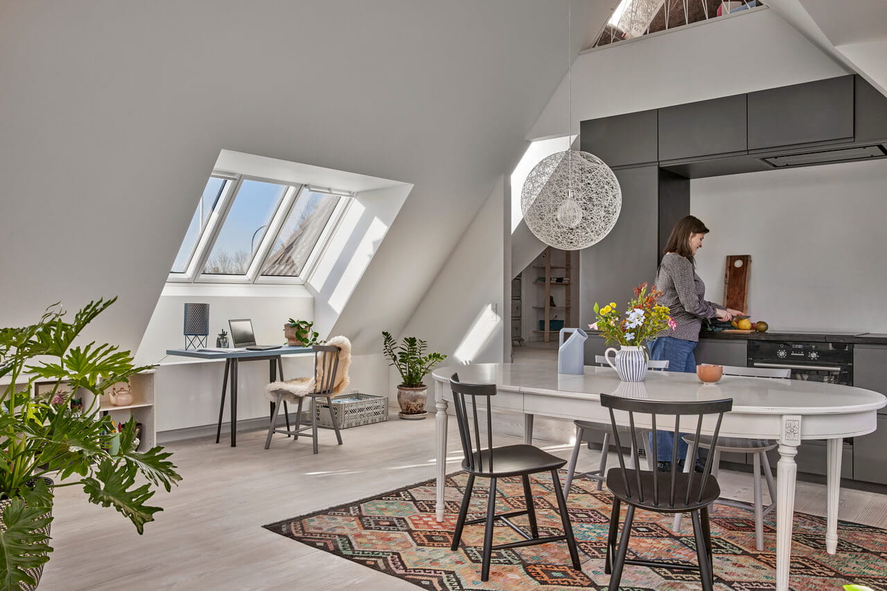 Kitchen and dining room area in the attic with woman standing and cutting fruit.