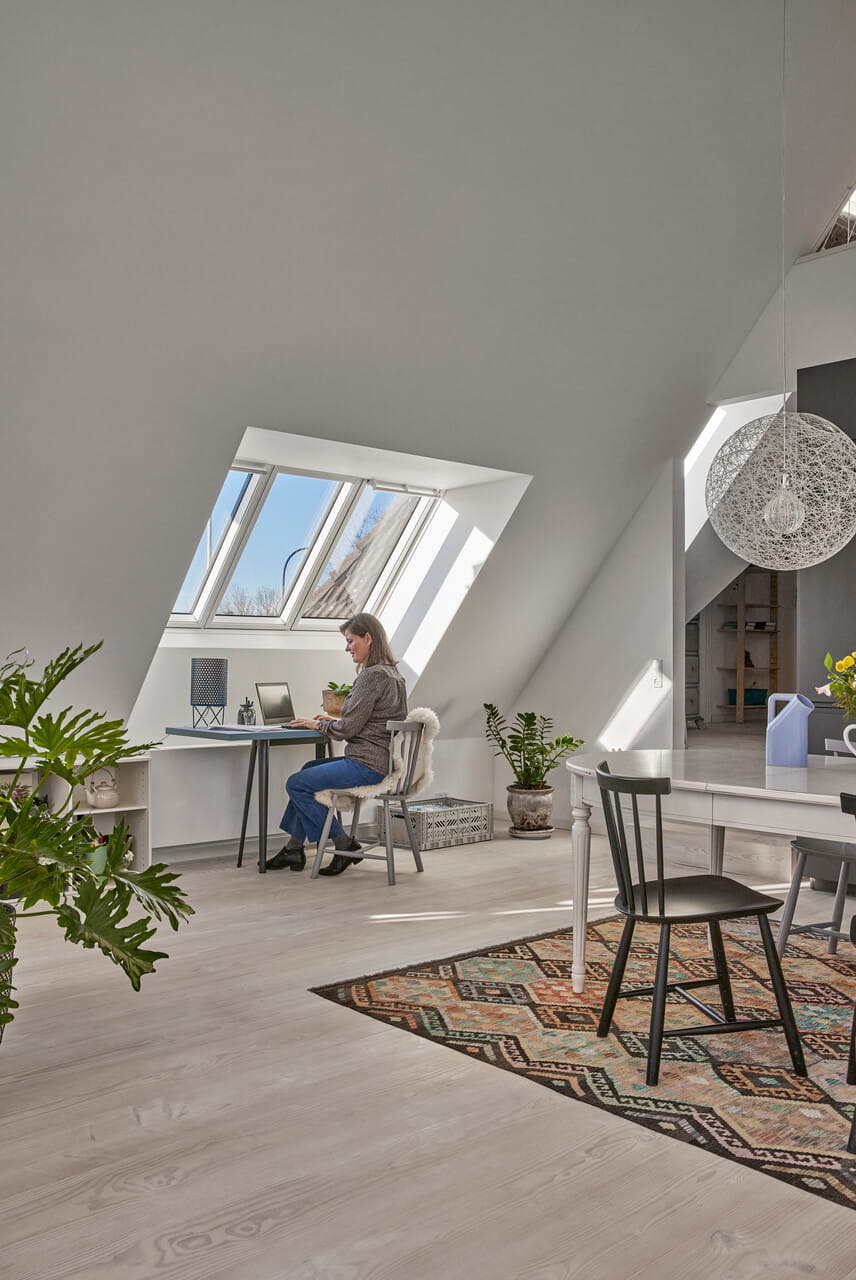 Spacious attic space with a home office area and woman sitting in it next to a table.