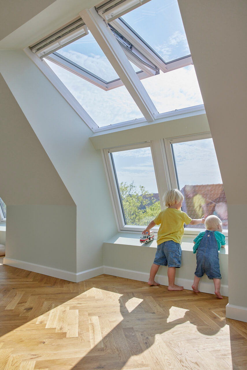 Two kids looking outside through a roof windows in the attic.