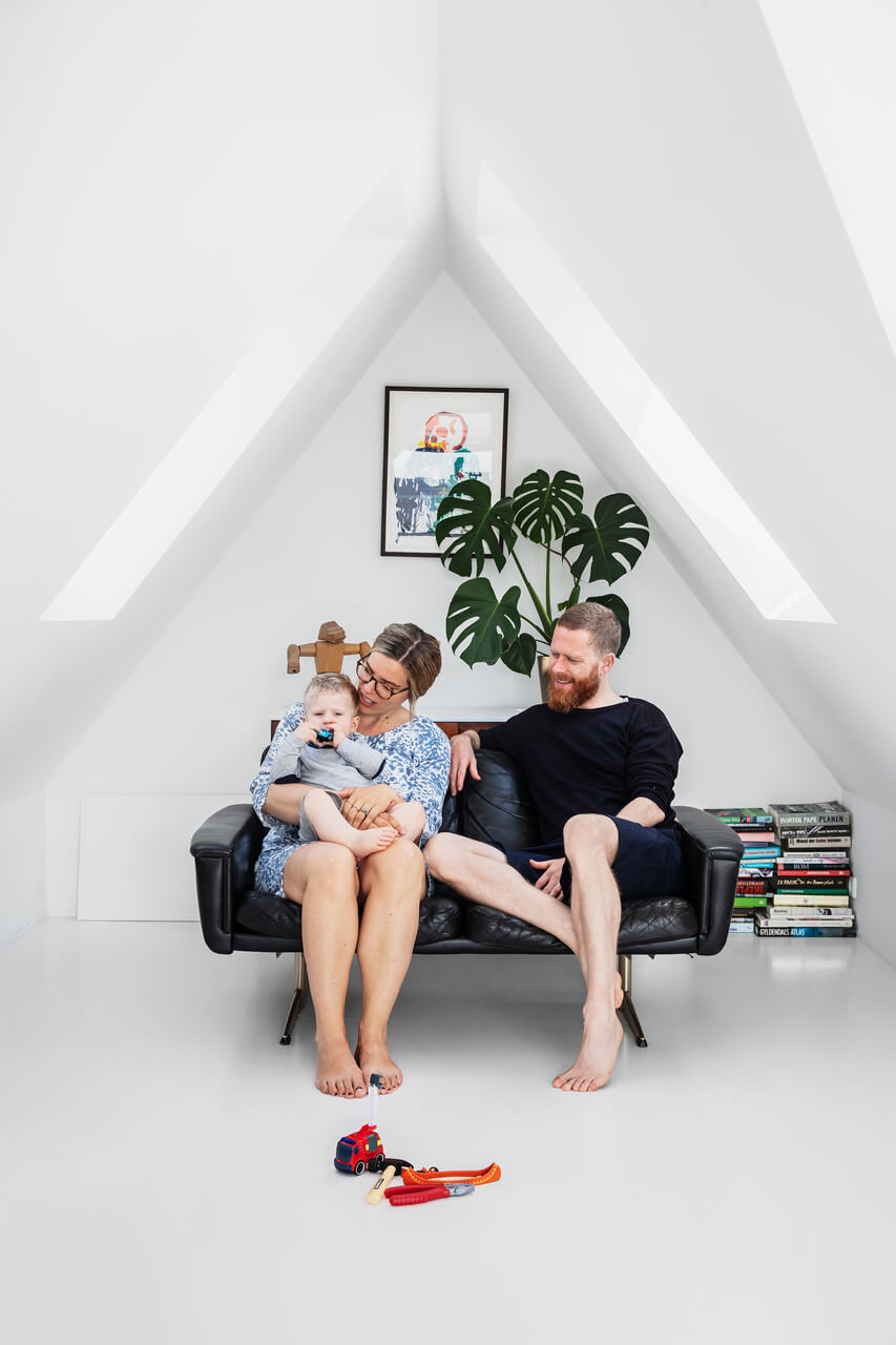 Two adults and a baby sitting on the black sofa in the attic.
