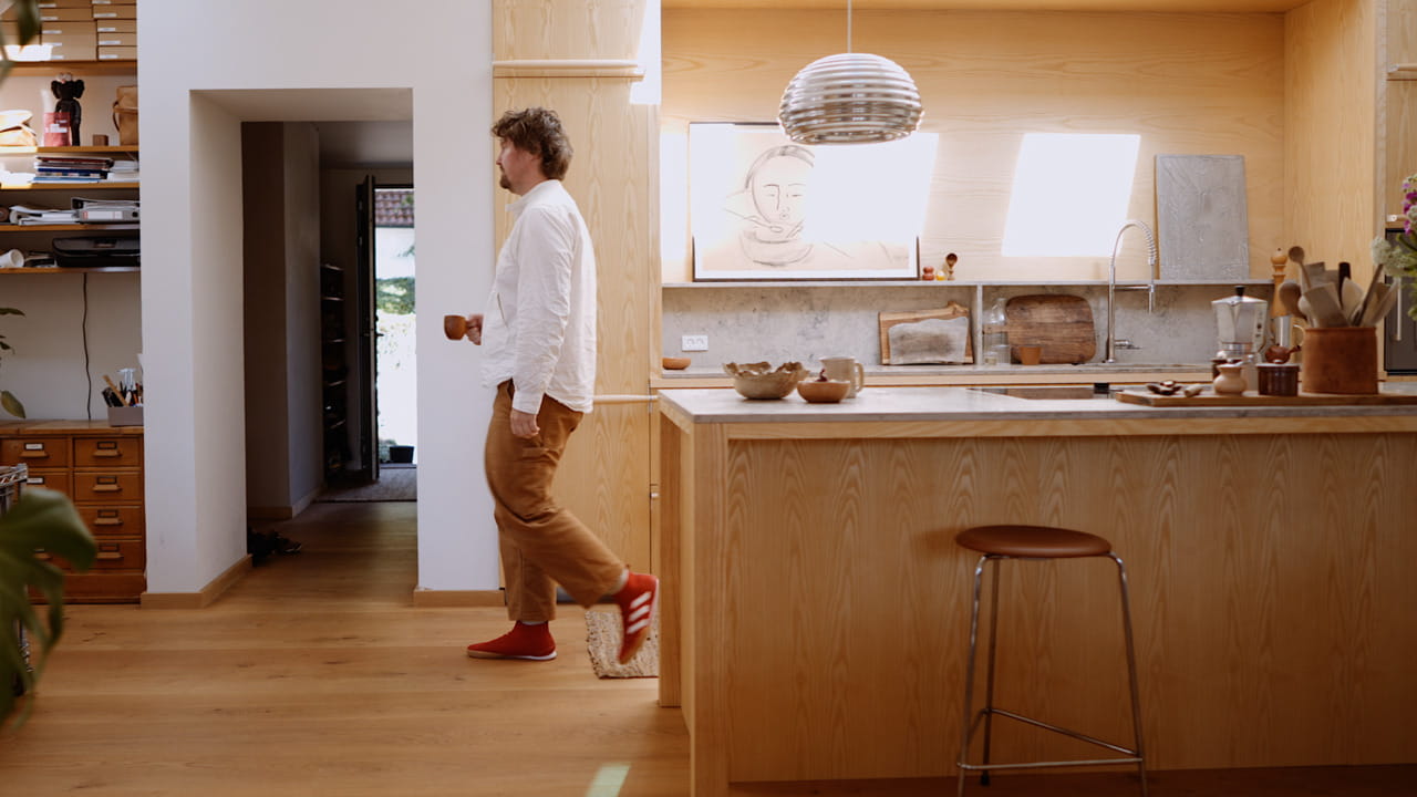 Man walking in the kitchen with a cup in his hand.