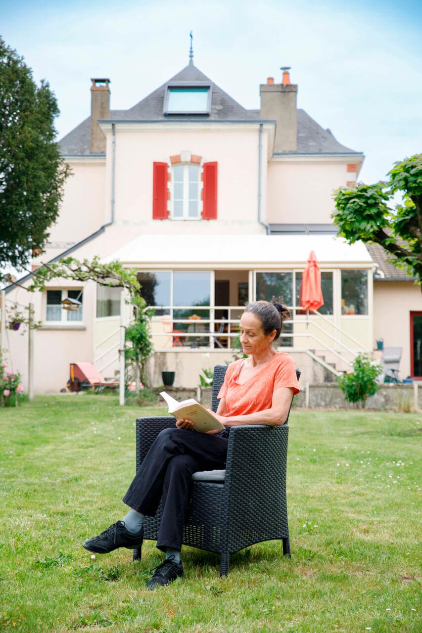 A woman sitting in the garden and reading a book in front of the nice house