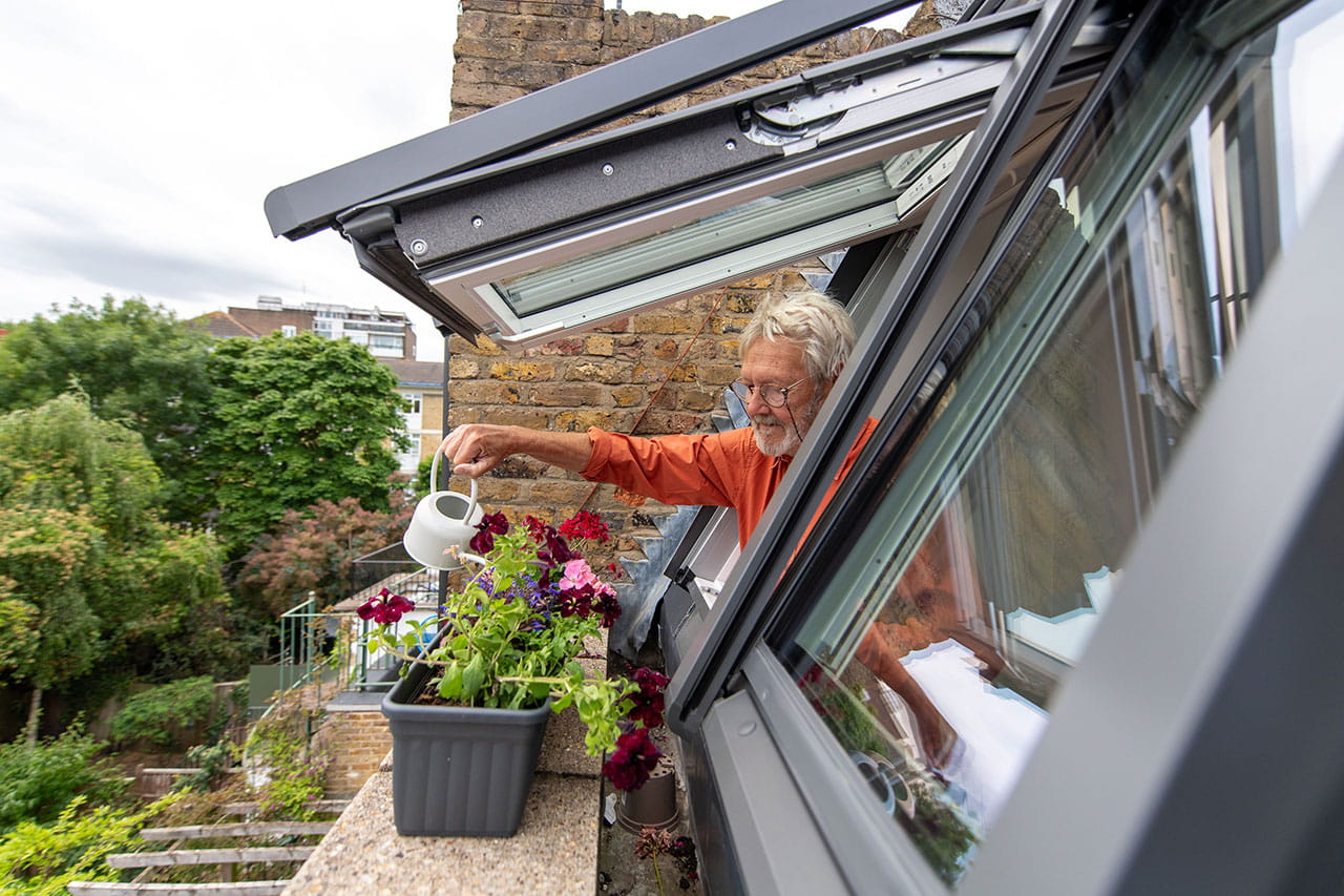 A hushed rooftop room in London-man watering plants from roof window