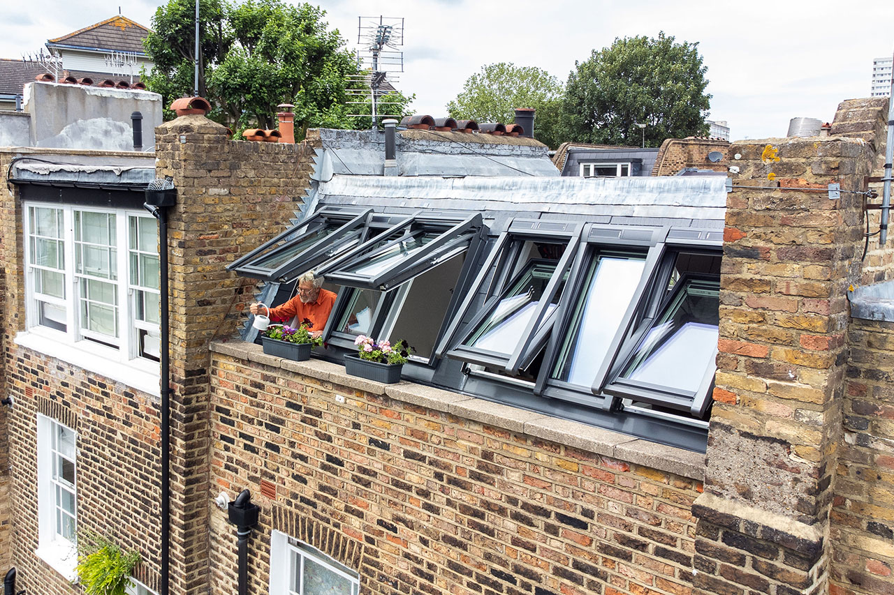 A hushed rooftop room in London-aerial external view man watering plants from roof window