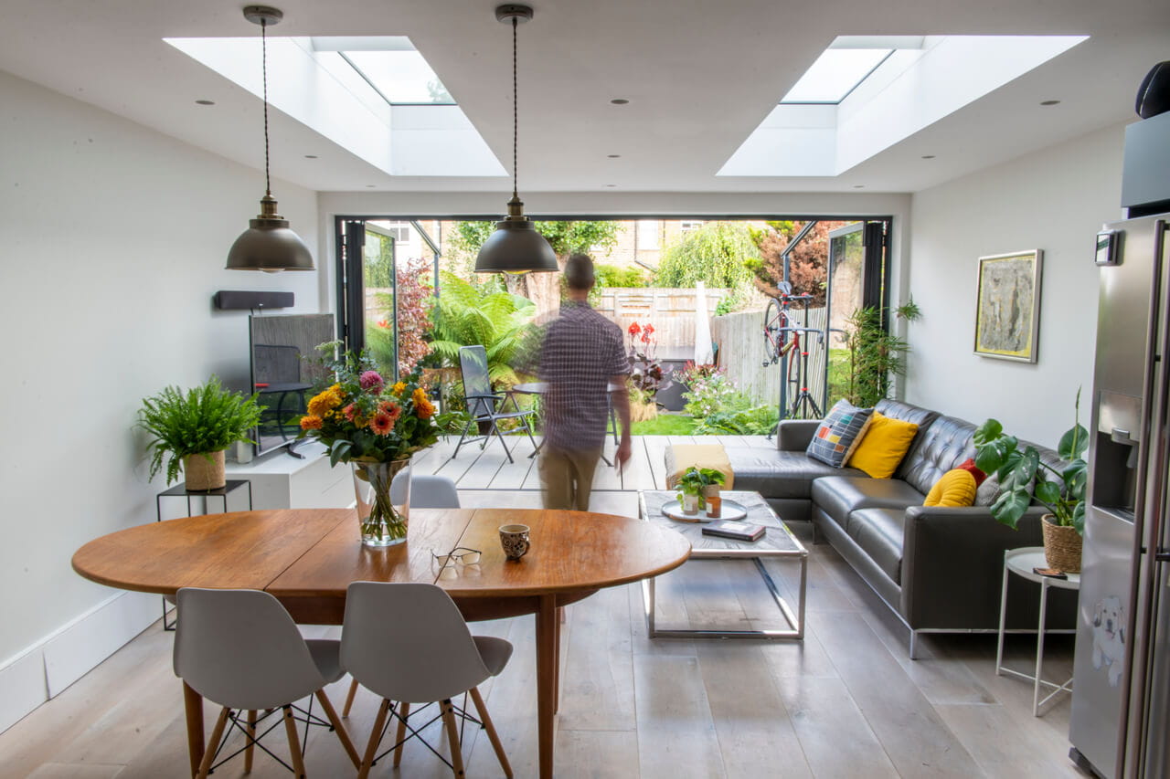 A dining room and living room area in the house extension with a man walking around it.