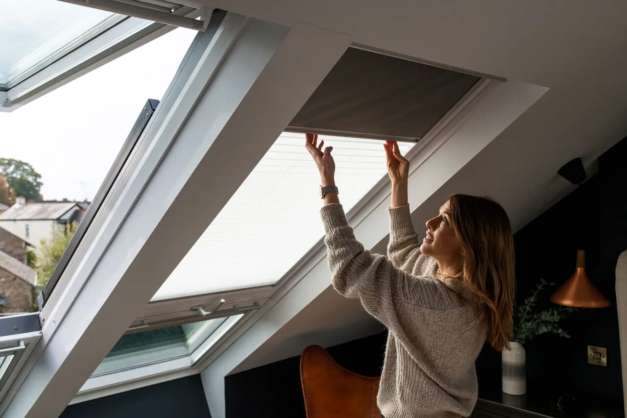 Woman closing down the blinds on VELUX roof window.