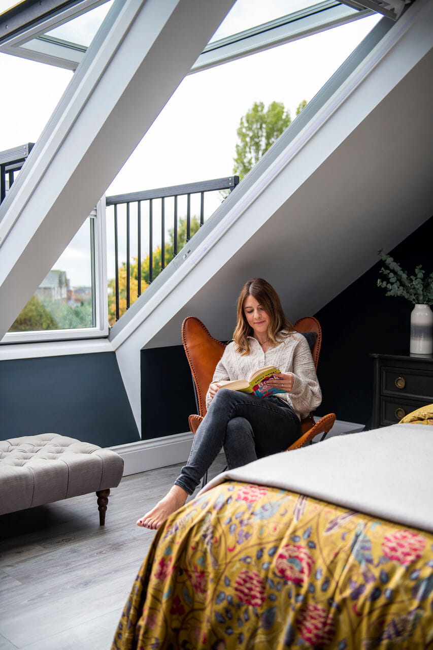 Woman sitting in the chair and reading in the bedroom by the side of roof window.