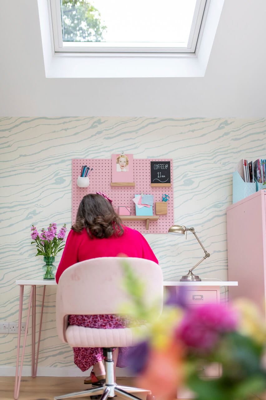 Woman sitting by the table on a pink chair.