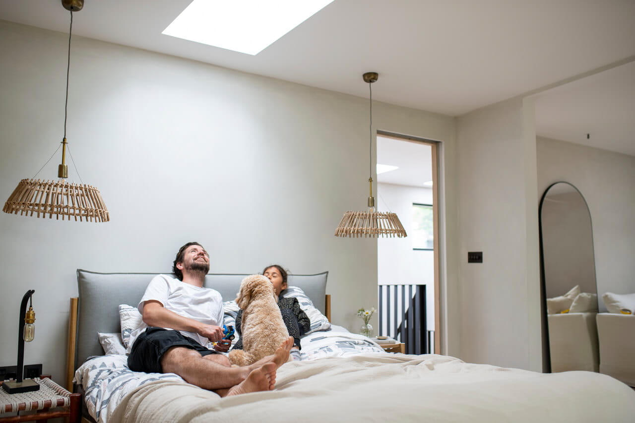 A family lying in the bed with a dog and looking up to the roof window
