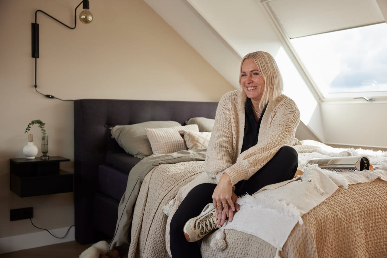Woman sitting on the bed in the bright bedroom with roof windows.
