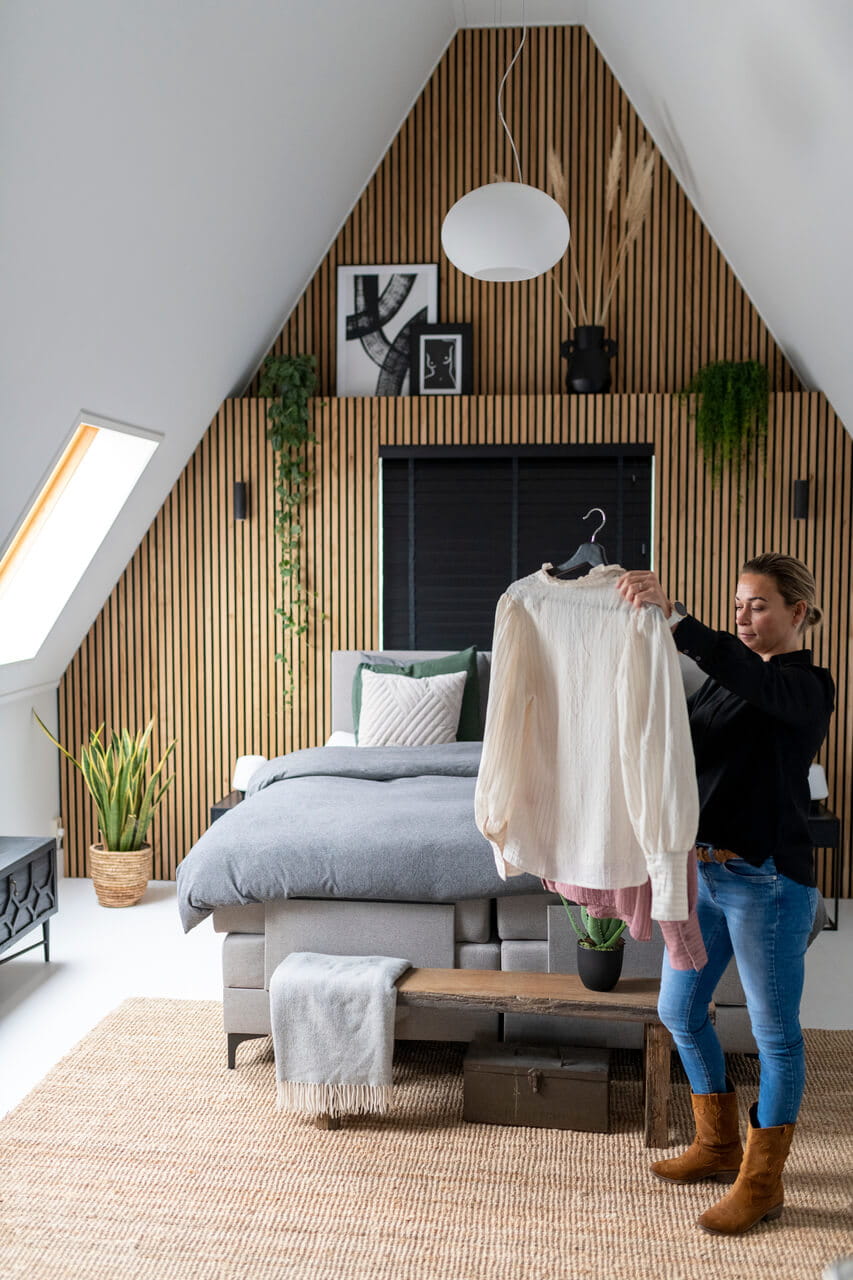Woman standing in the bedroom and holding a sweater on the hanger.