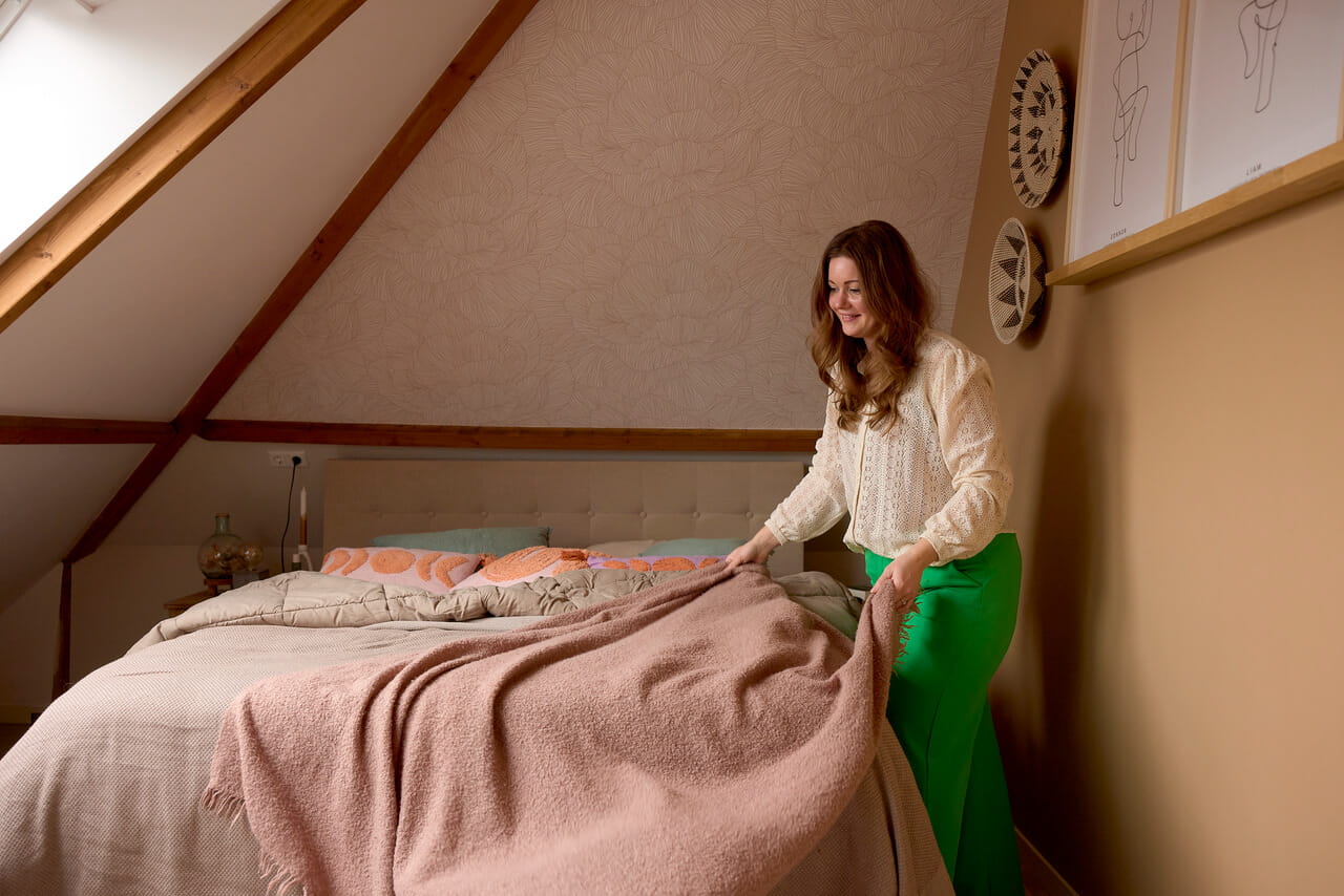 Woman in green pants making the bed.