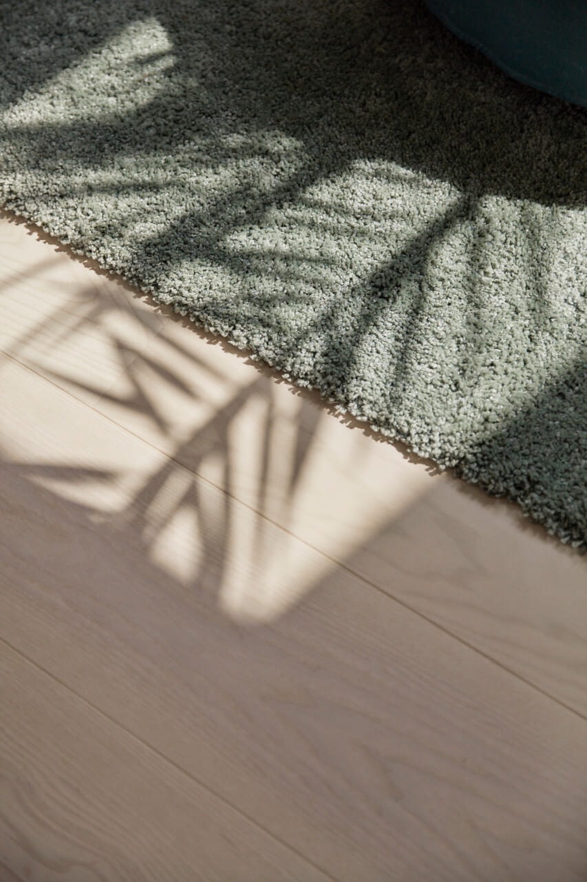 Image of wooden floor with green carpet and shadow falling on it.