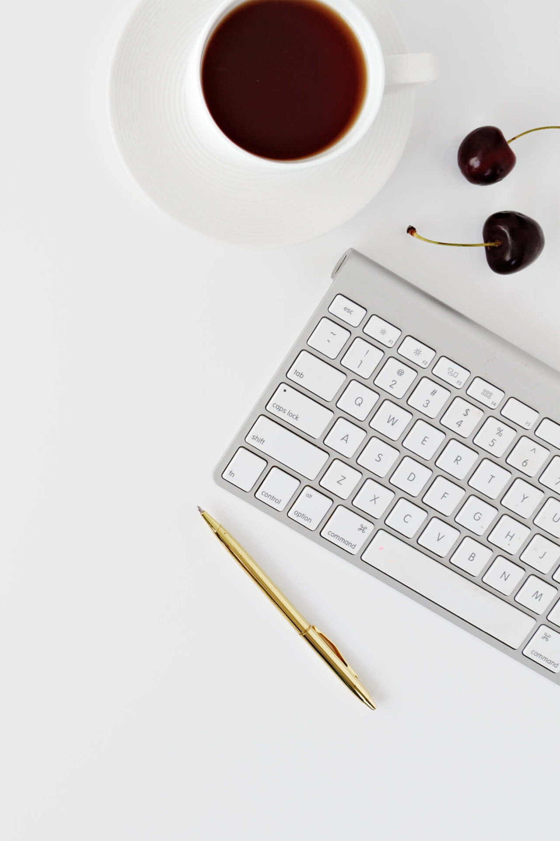 A keyboard, pen, coffee cup and two cherries on a white background